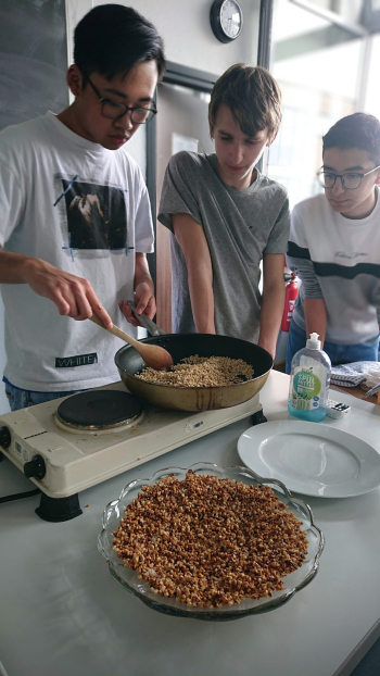 Man sieht drei Schüler, die an einer Herdplatte Essen zubereiten.